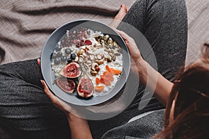 Woman in home clothes eating vegan Rice coconut porridge with figs, berries, nuts. Healthy breakfast ingredients