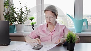 woman at home counting utility bills on a calculator, employee typing on her computer at her designated workstation, professional