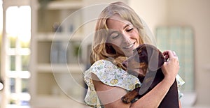 Woman At Home Holding And Stroking Pet Dachshund Dog In Kitchen