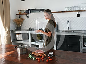 A woman at home in the kitchen prepares food using meat and vegetables, a large kitchen in a modern style, lifestyle