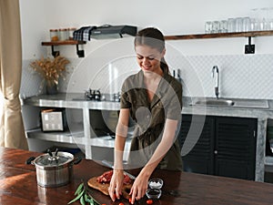 A woman at home in the kitchen prepares food using meat and vegetables, a large kitchen in a modern style, lifestyle