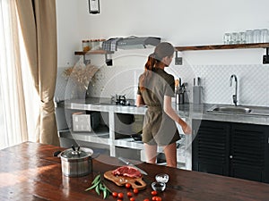 A woman at home in the kitchen prepares food using meat and vegetables, a large kitchen in a modern style, lifestyle