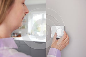 Woman At Home In Kitchen Turning Down Central Heating Thermostat To Save Energy And Money