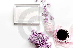 woman home office with lilic flowers frame and cup of coffee white desk background top view mock up