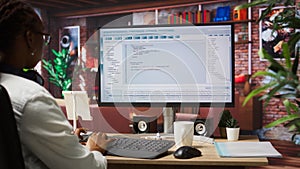 Woman in home office looking at UI on PC screen, typing code