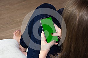 Woman at home relaxing reading on the smartphone with pre-keyed green screenn