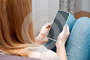 A woman at home sitting on the couch communicates with relatives via video call using a smartphone. Young woman making video call