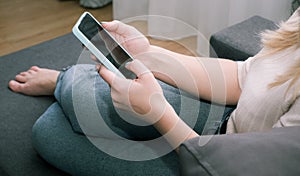 A woman at home sitting on the couch communicates with relatives via video call using a smartphone. Young woman making video call