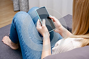 A woman at home sitting on the couch communicates with relatives via video call using a smartphone. Young woman making video call