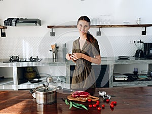 Woman at home smile in the kitchen prepares food using meat and vegetables, large modern style kitchen, lifestyle