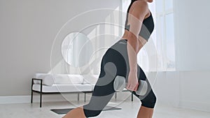 A woman at home on a Sunny day in the living room lunges back with dumbbells in her hands. Healthy lifestyle, daily