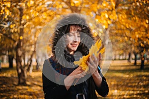 Woman in a hood with fur in the autumn forest. A girl in warm outerwear holds a bouquet of maple leaves