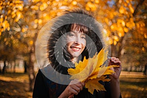 Woman in a hood with fur in the autumn forest. A girl in warm outerwear holds a bouquet of maple leaves