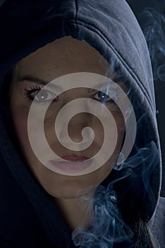 Woman with hood and smoke in darkness