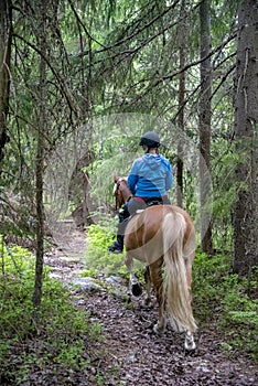 Woman horseback riding in forest path