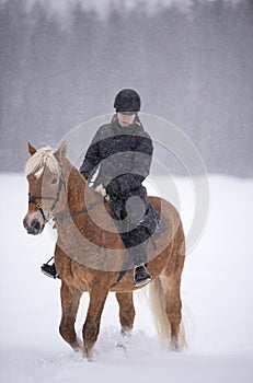 Woman horseback riding in winter snowfall