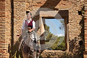 Woman horsewoman, young and beautiful, standing, riding her horse, in the field next to a ruined building. Concept horse riding,