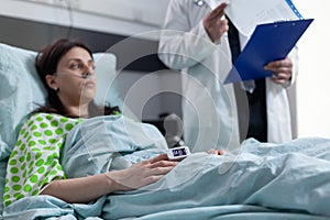 Woman on hospital bed with pulse oximeter on finger showing low oxygen saturation listening to doctor