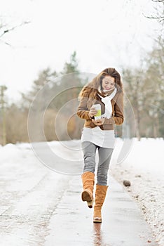 Woman with hot beverage walking in winter park