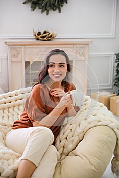 Woman with hot drink resting in comfortable papasan chair at home