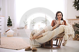 Woman with hot drink resting in comfortable papasan chair at home. Space for text