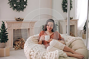 Woman with hot drink resting in comfortable papasan chair at home photo
