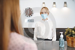 Woman hotel receptionist wearing medical mask to protect from coronavirus infection