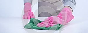 Woman housekeeper wearing protective gloves and using rag to wipe clean the table surface