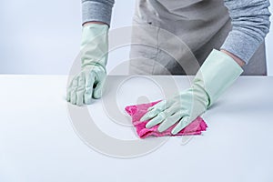 Woman housekeeper wearing protective gloves and using rag to wipe clean the table surface