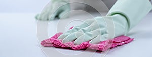 Woman housekeeper wearing protective gloves and using rag to wipe clean the table surface