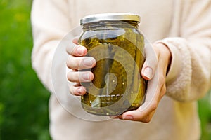 Woman housewife hand holding glass jar of pickled cucumbers. Domestic preparation pickling and canning of vegetables