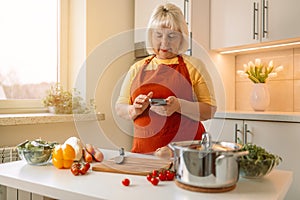 Woman housewife holds phone using cooking apps websites search recipes, chatting with friend during food preparation