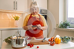 Woman housewife holds phone using cooking apps websites search recipes, chatting with friend during food preparation