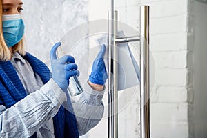 Woman Houseworker portrait in rubber blue gloves clean Door knob by cloth rag. Cleaning front door handle by antibacterial alcohol