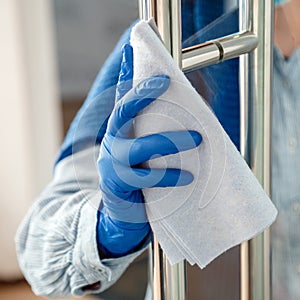 Woman Houseworker in rubber blue gloves clean Door knob by cloth rag. Cleaning front door handle by antibacterial alcohol spray.