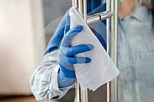 Woman Houseworker in rubber blue gloves clean Door knob by cloth rag. Cleaning front door handle by antibacterial alcohol spray.