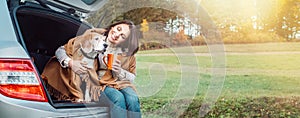 Woman huges her dog with shawls sitting together in car trunk