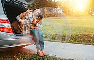 Woman huges her dog with shawls sitting together in car trunk