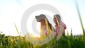 Woman hugging the dog at sunset and laughing, young girl with pet sitting on grass and resting in nature