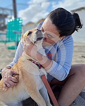 Woman hugging and kissing her dog on the beach