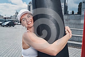 Woman is hugging punching bag and smiling