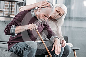 Woman hugging senior husband with walking stick at home