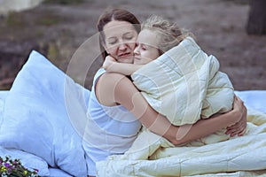 Woman hugs the child while sitting on the bed