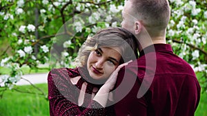 Woman hugs her husband. In the background flowering apple tree