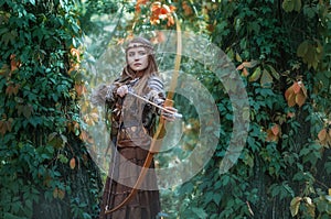 Woman hunter with a bow in hand, taking aim at his prey in the forest. Amazon.