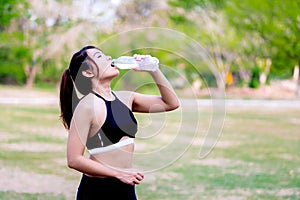 Woman hydrating post-workout in a park amidst greenery, embodying fitness and health. Teenage woman drinking water from a water