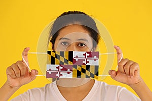 A woman and hygienic mask with Maryland flag pattern in her hand and raises it to cover her face. A mask is a very good protection