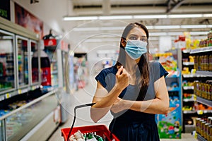 Woman with hygienic mask shopping for supplies and groceries. Shopper wearing a protective hygienic mask indoors. Pandemic