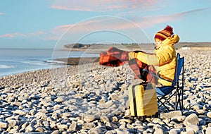 Woman i reaching the destination and sitting on beach chairs on the seaside at sunrise. British cold