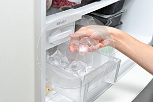 Woman with ice cubes from the freezer. An ice maker in a household refrigerator